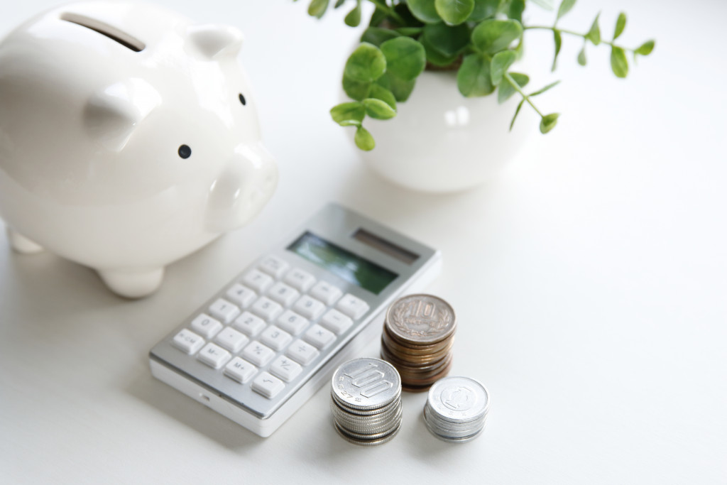 A white piggy bank, calculator, potted plant, and coins